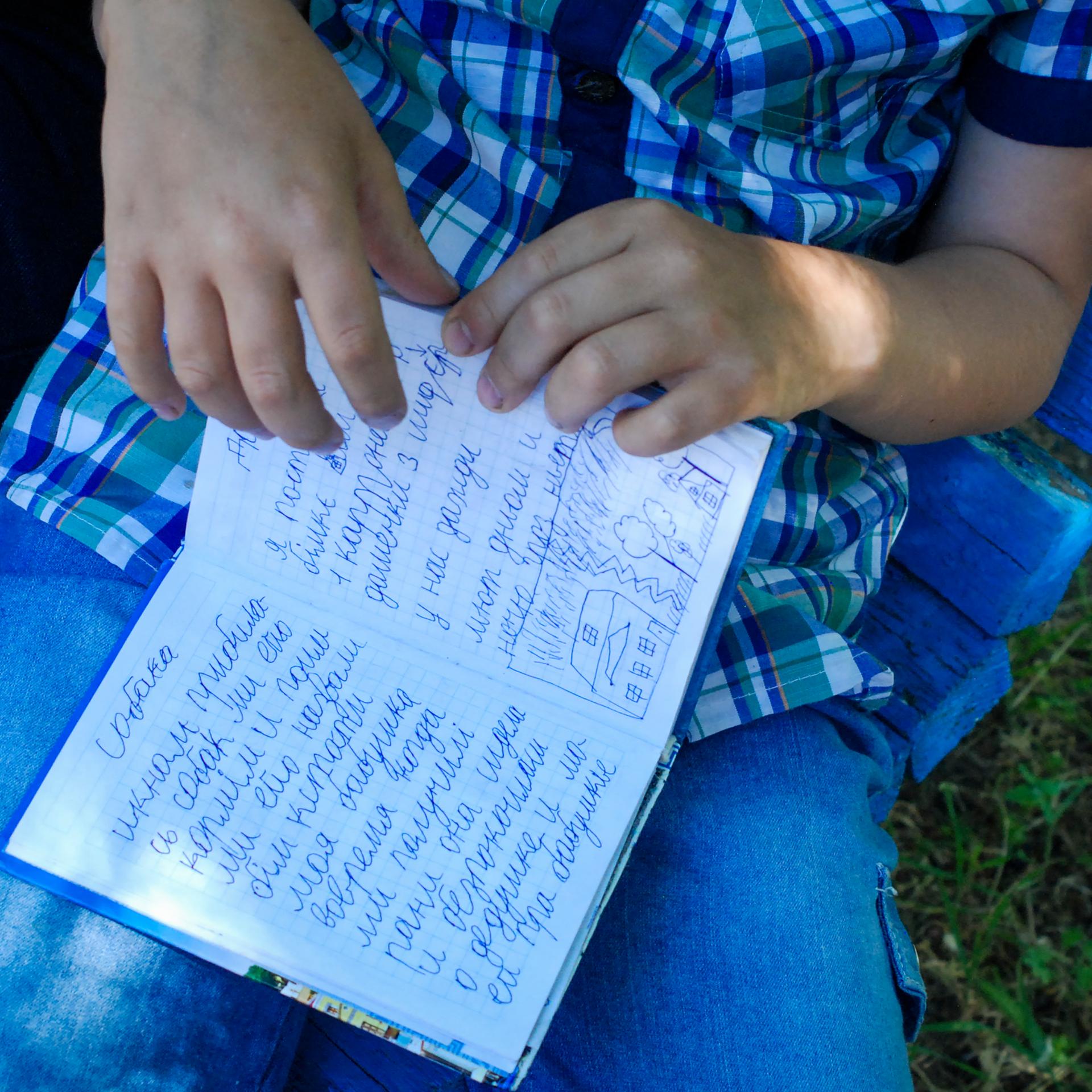 Der 8-Jährige Egor hält ein kleines blaues Buch in seiner Hand. Er hat in Mariupol Tagebuch geführt, als die Stadt blutig umkämpft war. Auf der aufgeschlagenen Seite steht neben einer kleinen Zeichnung: "Ich habe gut geschlafen, habe gelächelt und 25 Seiten gelesen. Ausserdem ist mein Grossvater gestorben am 26.April". Zaporizhzhia, 3.Juni 2022.