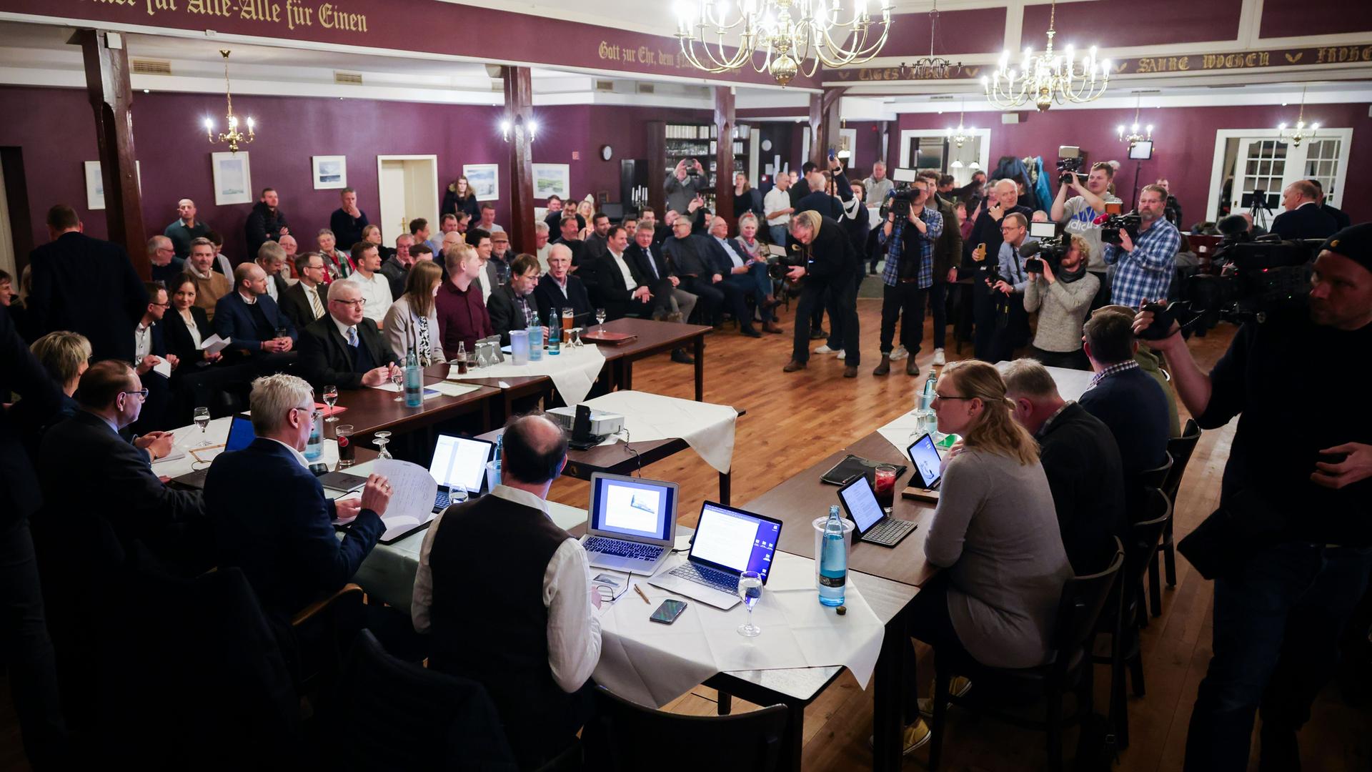 In einem Saal sitzen zahlreiche Menschen in einer Gemeinderatssitzung zusammen. Einige Journalisten machen Foto- und Filmaufnahmen. An der Decke hängen zwei große Lüster. In einem Saal sitzen zahlreiche Menschen in einer Gemeinderatssitzung zusammen. Einige Journalisten machen Foto- und Filmaufnahmen. An der Decke hängen zwei große Lüster.