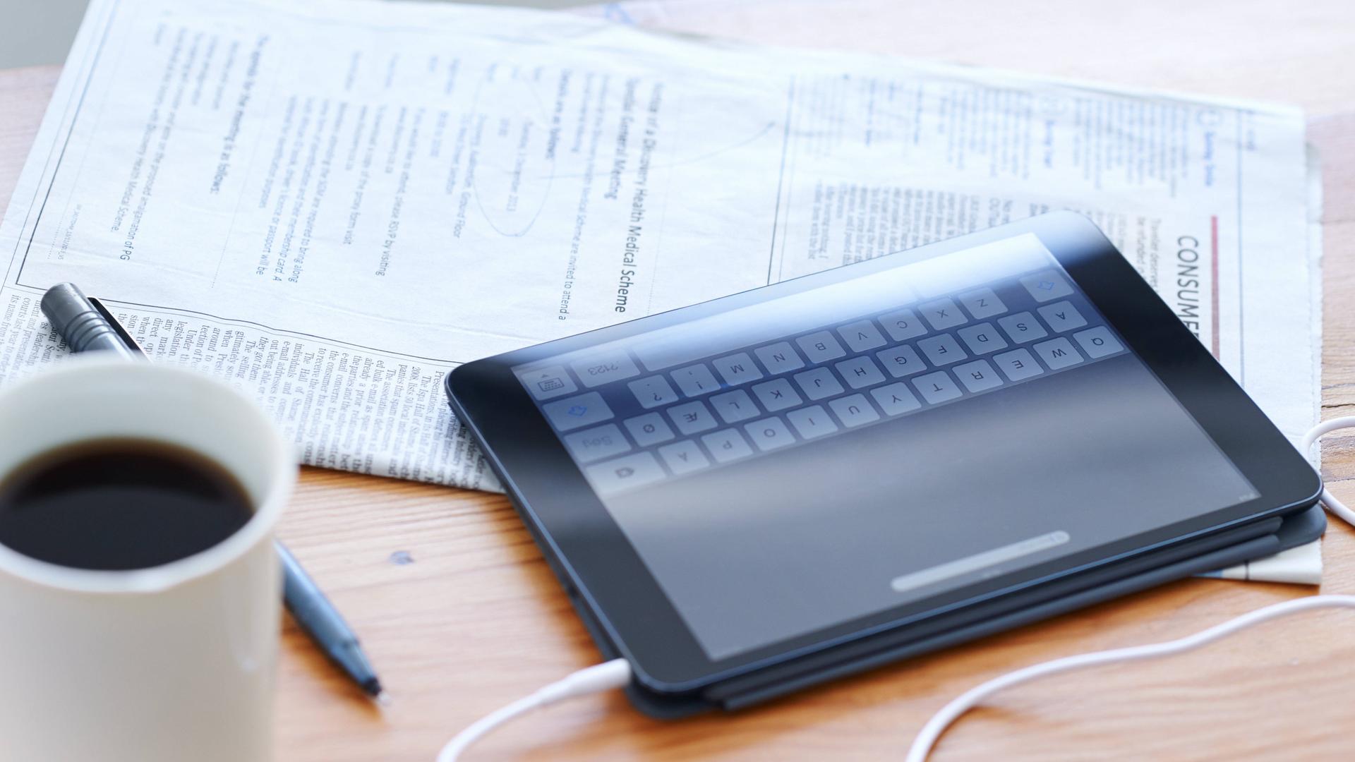 Eine Zeitung und ein Tablet liegen auf einem Tisch.