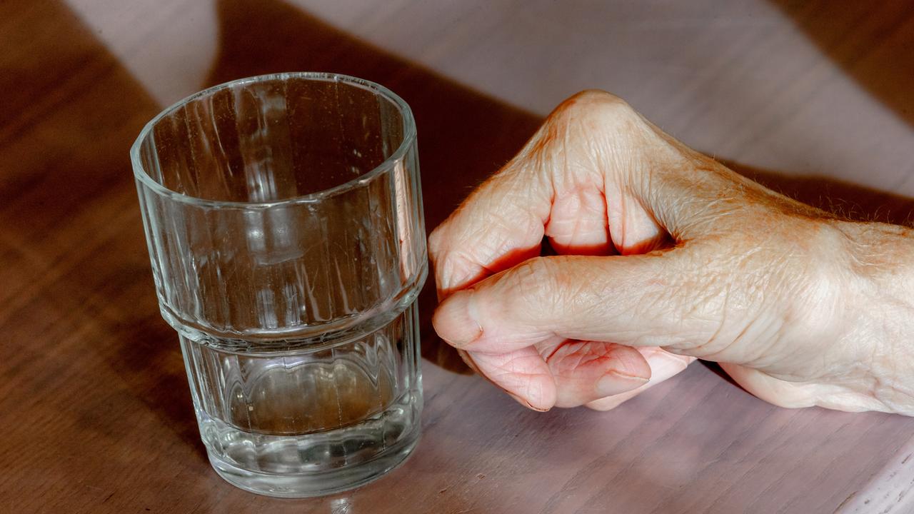 Die Hand einer alten Frau liegt neben einem leeren Wasserglas auf einem Tisch. Die Hand einer alten Frau liegt neben einem leeren Wasserglas auf einem Tisch.