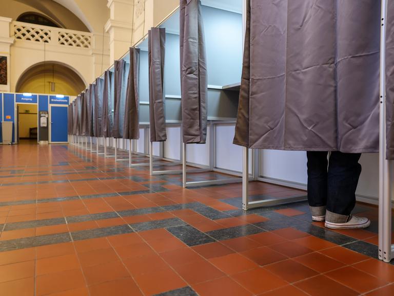 Ein Mann steht in einer Wahlkabine im Neuen Rathaus der Stadt Leipzig.