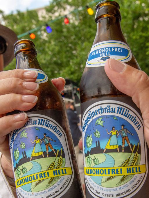 Zwei Personen stoßen in Münchens erstem akoholfreien Biergarten mit alkoholfreiem Augustiner Helles an.