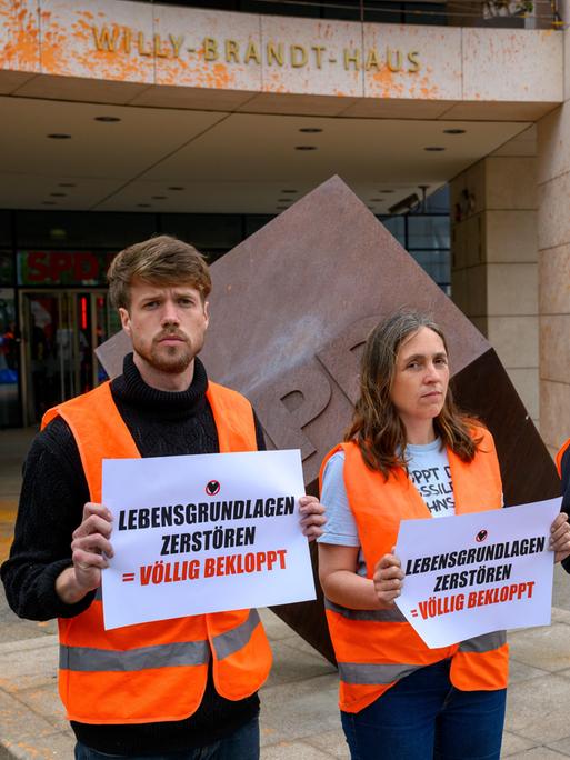 Menschen stehen mit Zetteln vor einem Gebäude.