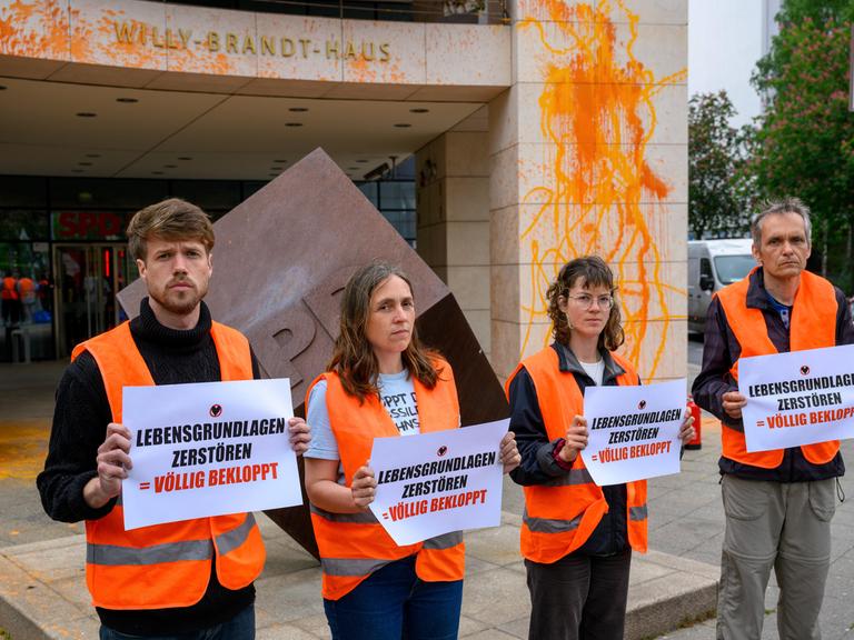 Menschen stehen mit Zetteln vor einem Gebäude.