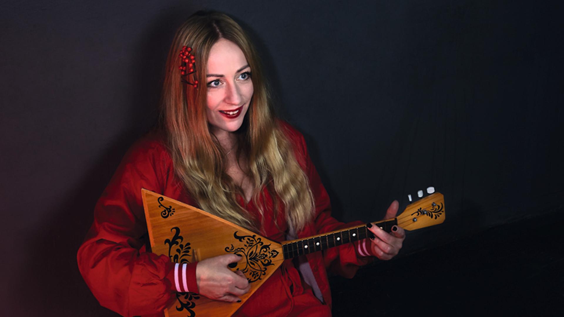 Doreen Kutzke hält ein Saiteninstrument in der Hand und hat die Beine nach vorne ausgestreckt. Sie träg ein weinrotes Kleid, hat lange Haare mit einem Mittelscheitel. Doreen Kutzke hält ein Saiteninstrument in der Hand und hat die Beine nach vorne ausgestreckt. Sie träg ein weinrotes Kleid, hat lange Haare mit einem Mittelscheitel.