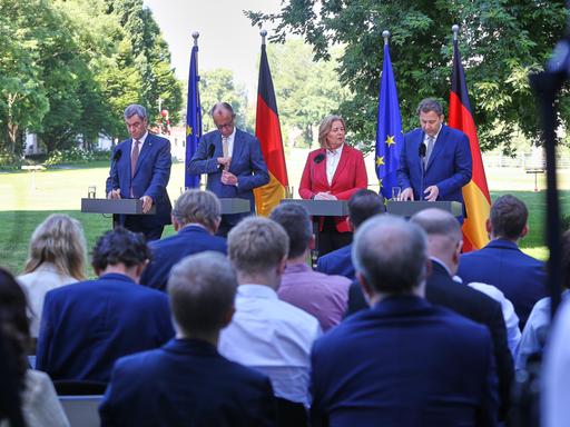 Bayerns Ministerpräsident Markus Söder (CSU), Bundeskanzler Friedrich Merz (CDU), Arbeitsministerin Bärbel Bas (SPD), Finanzminister Lars Klingbeil (SPD) stehen an vier Stehtischen im Grünen und geben eine Pressekonferenz. Bayerns Ministerpräsident Markus Söder (CSU), Bundeskanzler Friedrich Merz (CDU), Arbeitsministerin Bärbel Bas (SPD), Finanzminister Lars Klingbeil (SPD) stehen an vier Stehtischen im Grünen und geben eine Pressekonferenz.