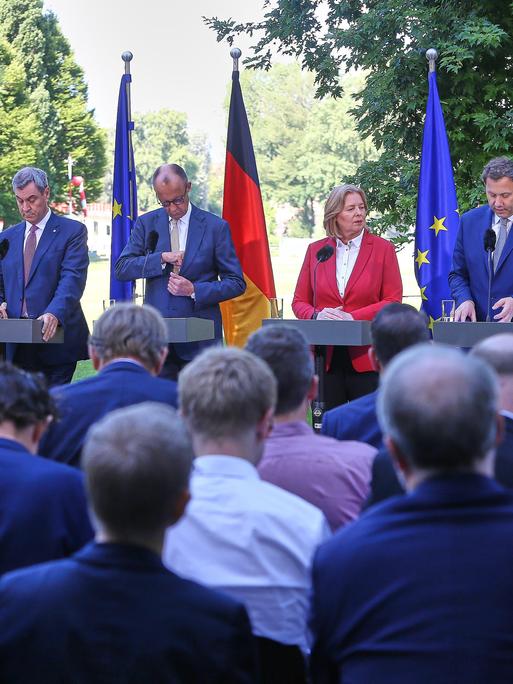 Bayerns Ministerpräsident Markus Söder (CSU), Bundeskanzler Friedrich Merz (CDU), Arbeitsministerin Bärbel Bas (SPD), Finanzminister Lars Klingbeil (SPD) stehen an vier Stehtischen im Grünen und geben eine Pressekonferenz.