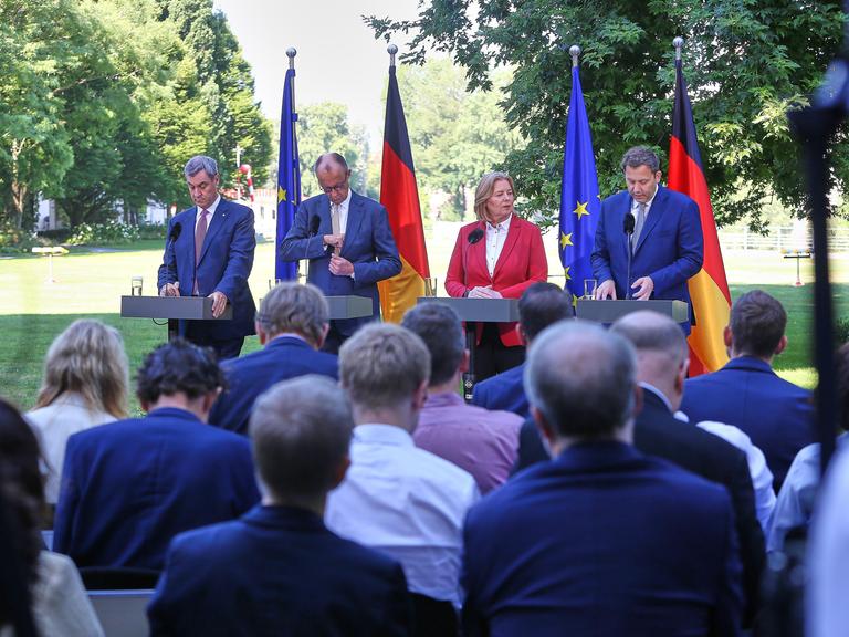 Bayerns Ministerpräsident Markus Söder (CSU), Bundeskanzler Friedrich Merz (CDU), Arbeitsministerin Bärbel Bas (SPD), Finanzminister Lars Klingbeil (SPD) stehen an vier Stehtischen im Grünen und geben eine Pressekonferenz.