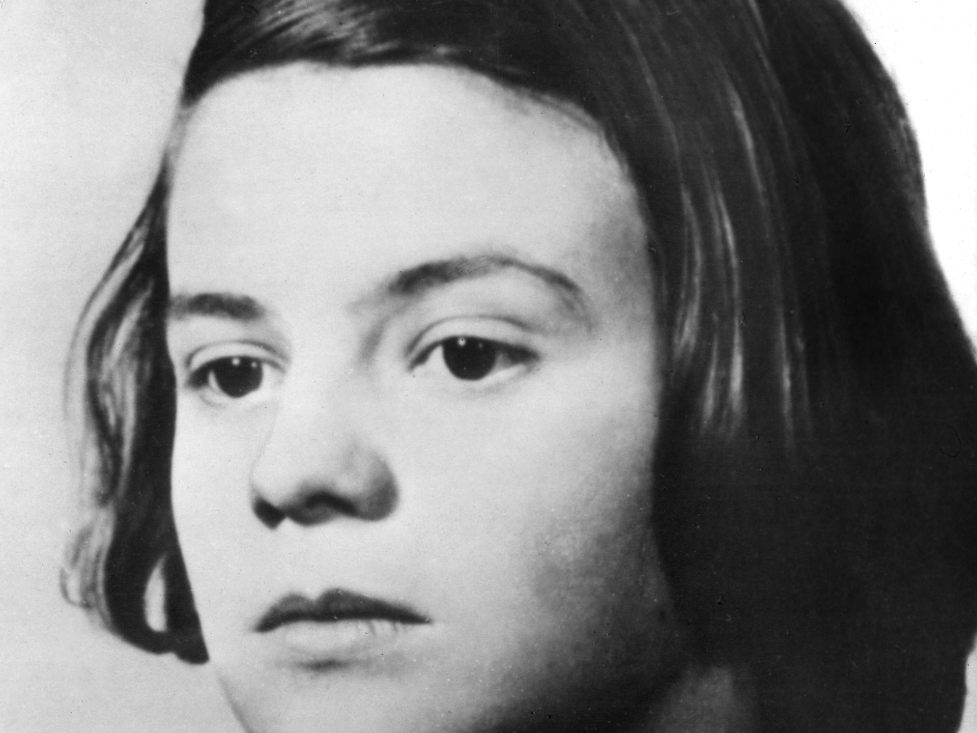 Undatierte Porträtaufnahme von Sophie Scholl. Sie hat dunkle Haare und trägt einen Seitenscheitel, ihr Oberteil ist auch von dunkler Farbe. Undatierte Porträtaufnahme von Sophie Scholl. Sie hat dunkle Haare und trägt einen Seitenscheitel, ihr Oberteil ist auch von dunkler Farbe.