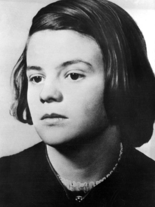 Undatierte Porträtaufnahme von Sophie Scholl. Sie hat dunkle Haare und trägt einen Seitenscheitel, ihr Oberteil ist auch von dunkler Farbe.