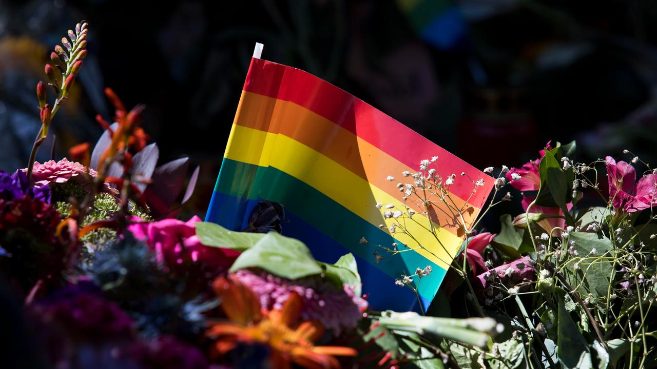 Regenbogenfahne inmitten von Blumen und Kerzen