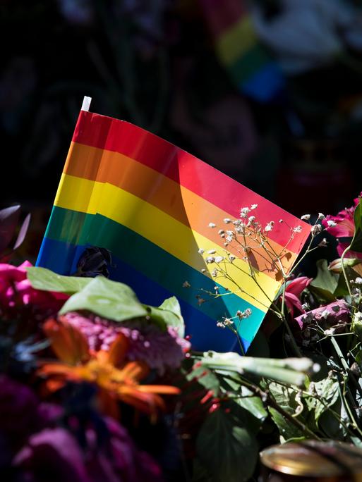 Regenbogenfahne inmitten von Blumen und Kerzen