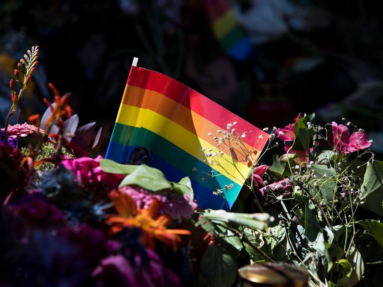 Regenbogenfahne inmitten von Blumen und Kerzen