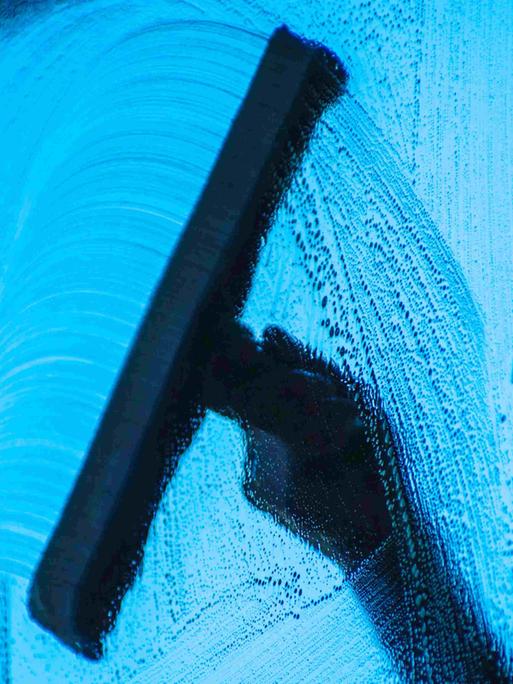 Bild aus dem Auto heraus fotografiert: Eine Hand wischt mit einem Wischer die Scheibe eines Autos.