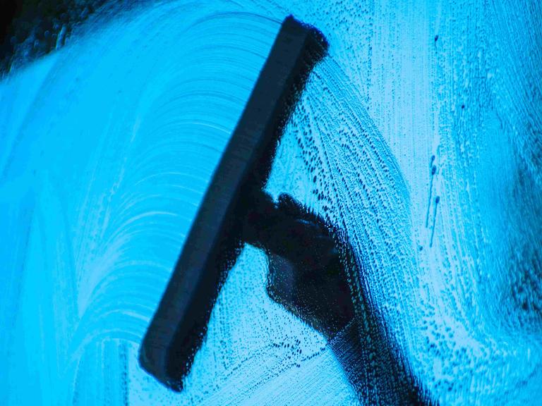 Bild aus dem Auto heraus fotografiert: Eine Hand wischt mit einem Wischer die Scheibe eines Autos.