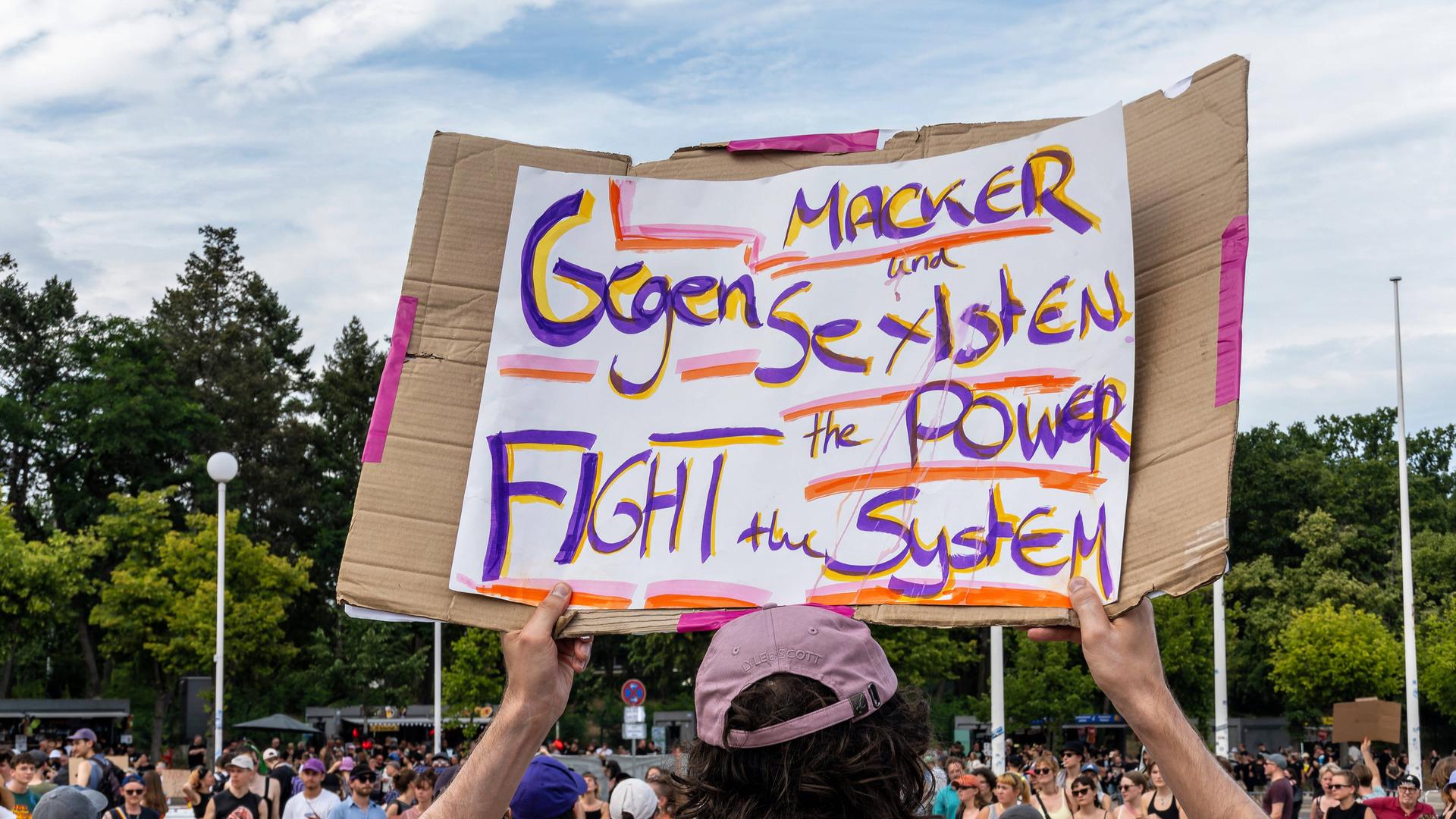 Im Umfeld des Berlin-Konzerts der Band Rammstein am 15. Juli 2023 hält eine Person, die nur von hinten zu sehen ist, ein Transparent in die Höhe: Darauf steht: "Gegen Macker und Sexisten: Fight the Power, the System"