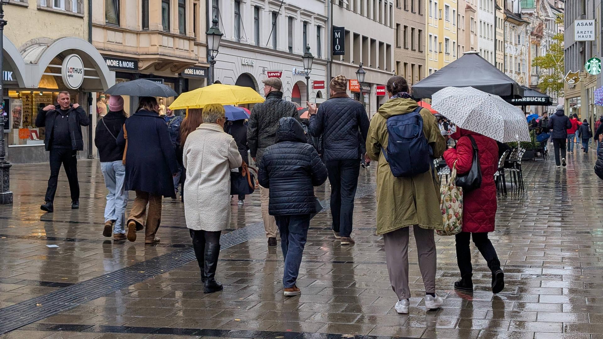 Menschen mit Regenschirmen gehen durch eine Münchener Fußgängerzone Menschen mit Regenschirmen gehen durch eine Münchener Fußgängerzone