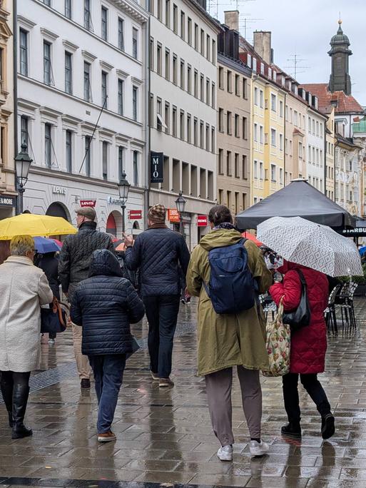 Menschen mit Regenschirmen gehen durch eine Münchener Fußgängerzone