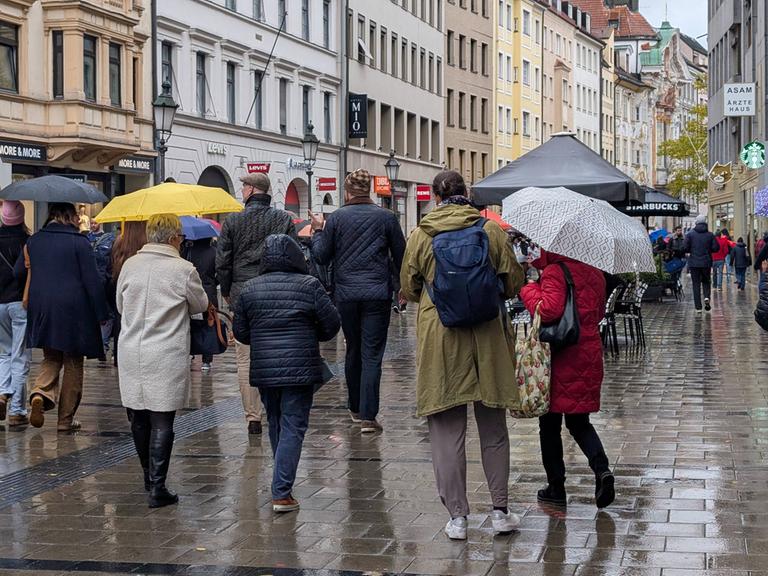 Menschen mit Regenschirmen gehen durch eine Münchener Fußgängerzone