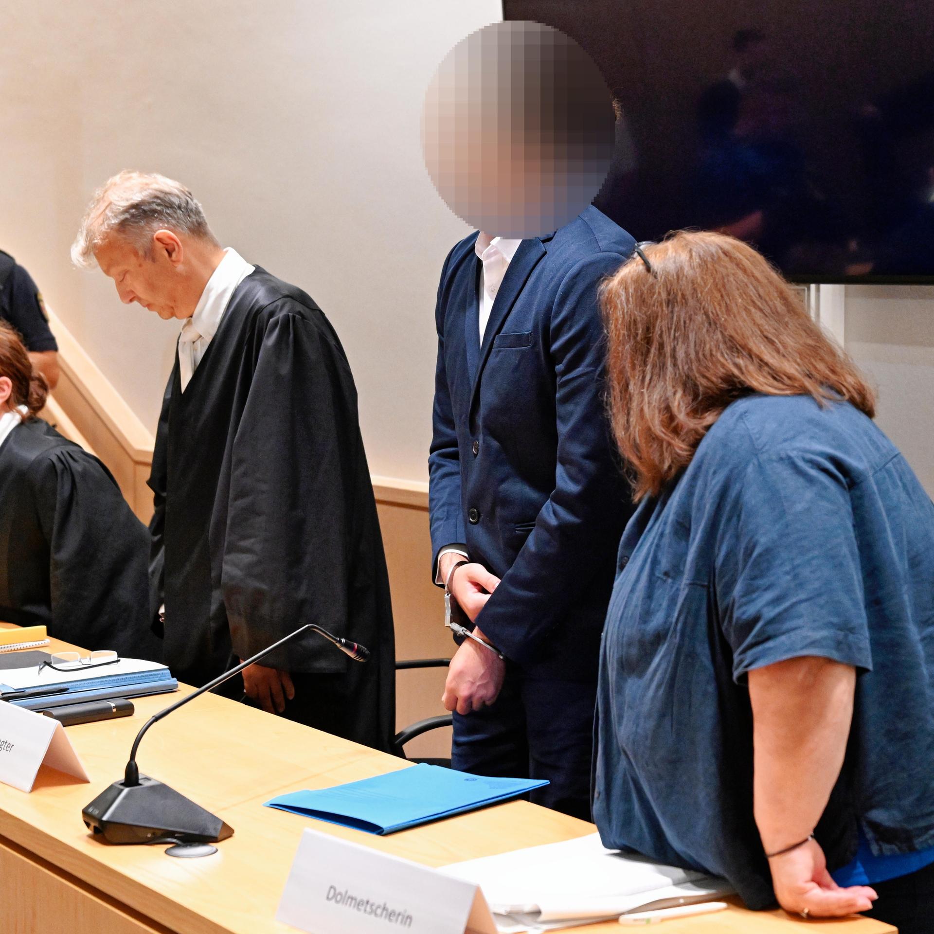 Der Angeklagte (2.v.r.) steht neben seinen Anwälten und der Dolmetscherin im Verhandlungssaal des Landgerichts.