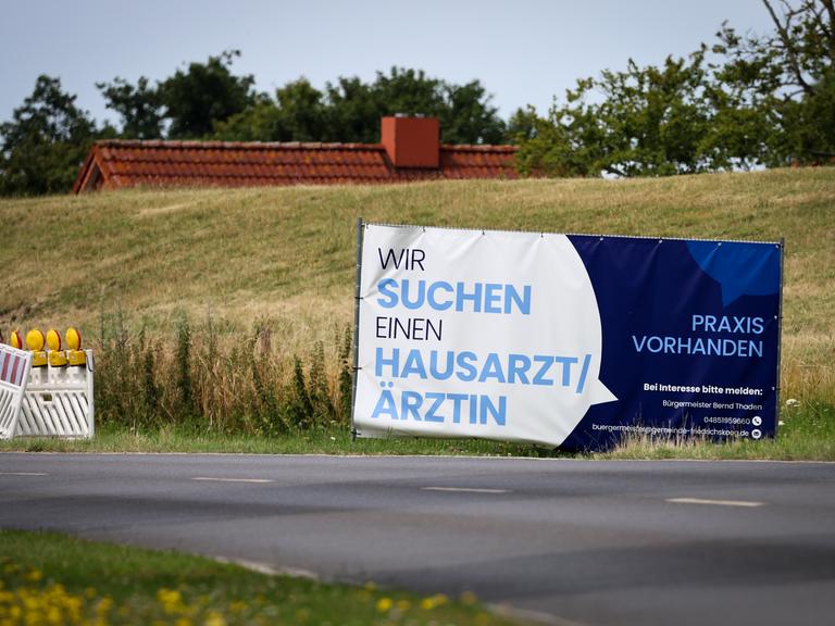 Mit einem Plakat wird in einer ländlichen Region in Schleswig-Holstein nach Ärzten und Ärztinnen gesucht. 