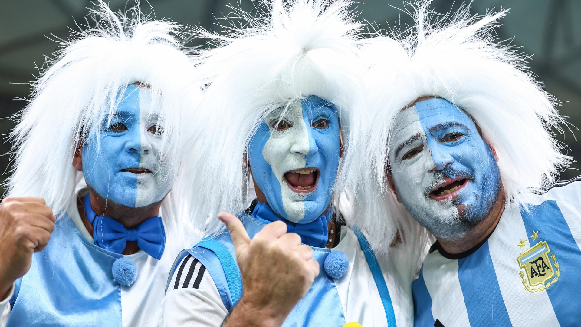 Blauweiß im Gesicht angemalte argentinische Fans mit weißen Perücken bei der Fußball-WM in Katar.