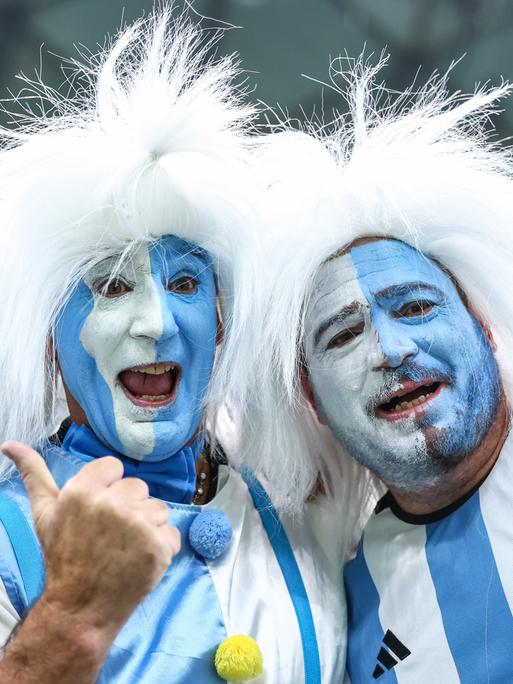 Blauweiß im Gesicht angemalte argentinische Fans mit weißen Perücken bei der Fußball-WM in Katar.