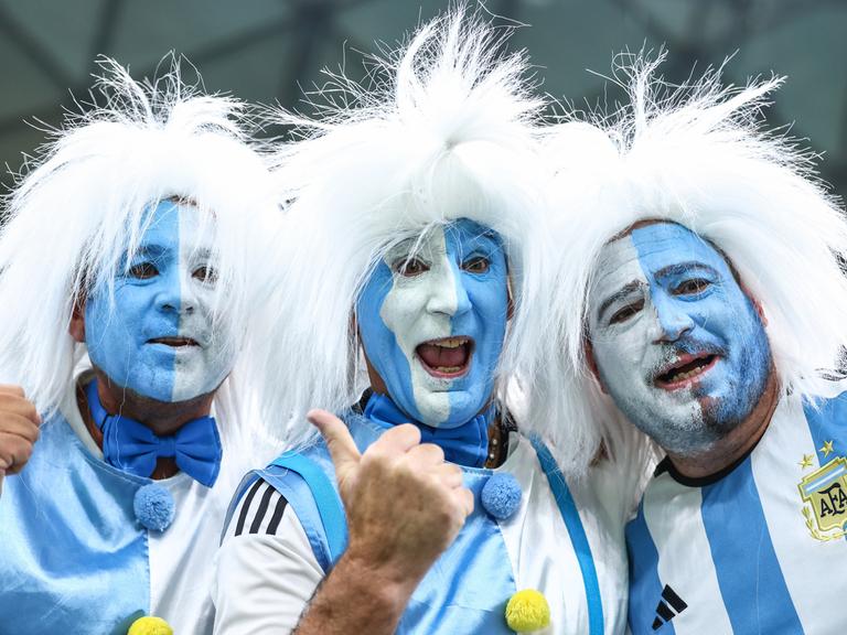Blauweiß im Gesicht angemalte argentinische Fans mit weißen Perücken bei der Fußball-WM in Katar.