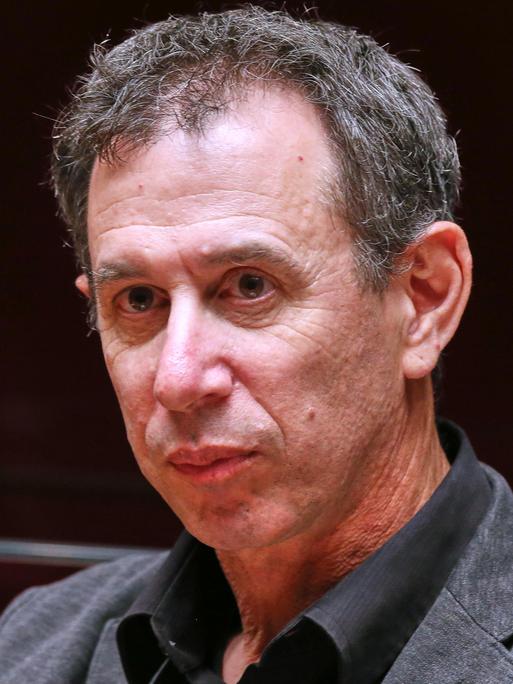 Portrait von Assaf Gavron, der vor einem dunklen Hintergrund sitzt und an der Kamera vorbeischaut.