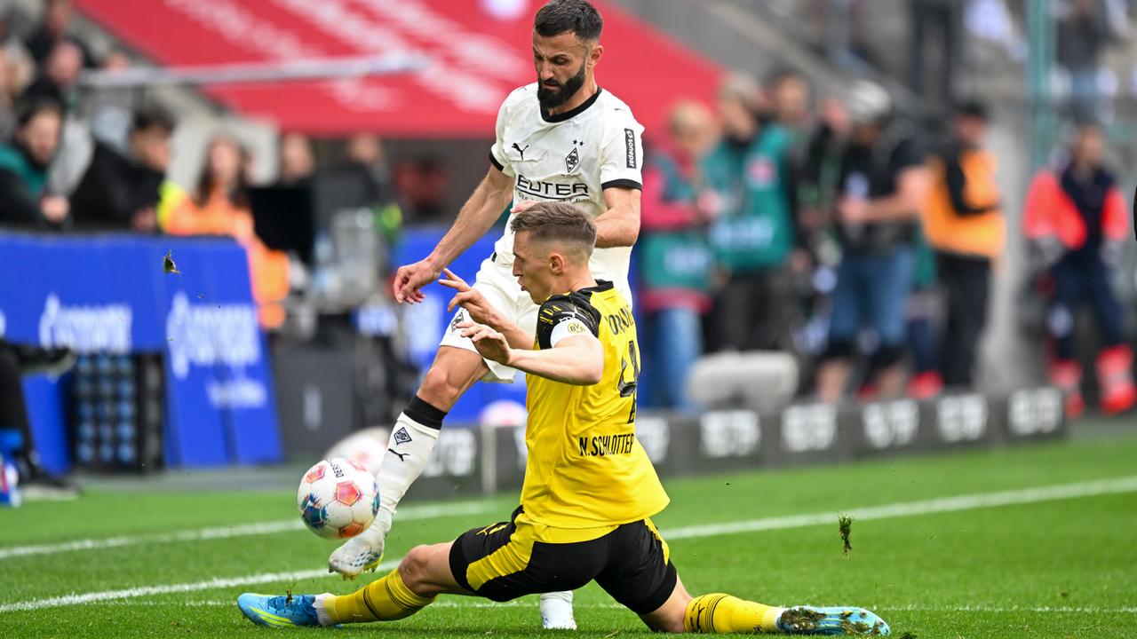 Der Fußballer Nico Schlotterbeck (Borussia Dortmund) grätscht vor dem Spieler Franck Honorat (Borussia Mönchengladbach) und versucht den Ball zu treffen.