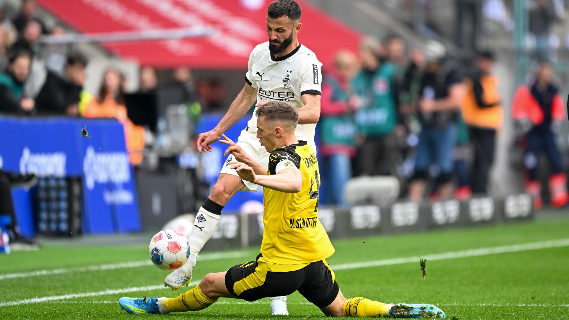 Der Fußballer Nico Schlotterbeck (Borussia Dortmund) grätscht vor dem Spieler Franck Honorat (Borussia Mönchengladbach) und versucht den Ball zu treffen.