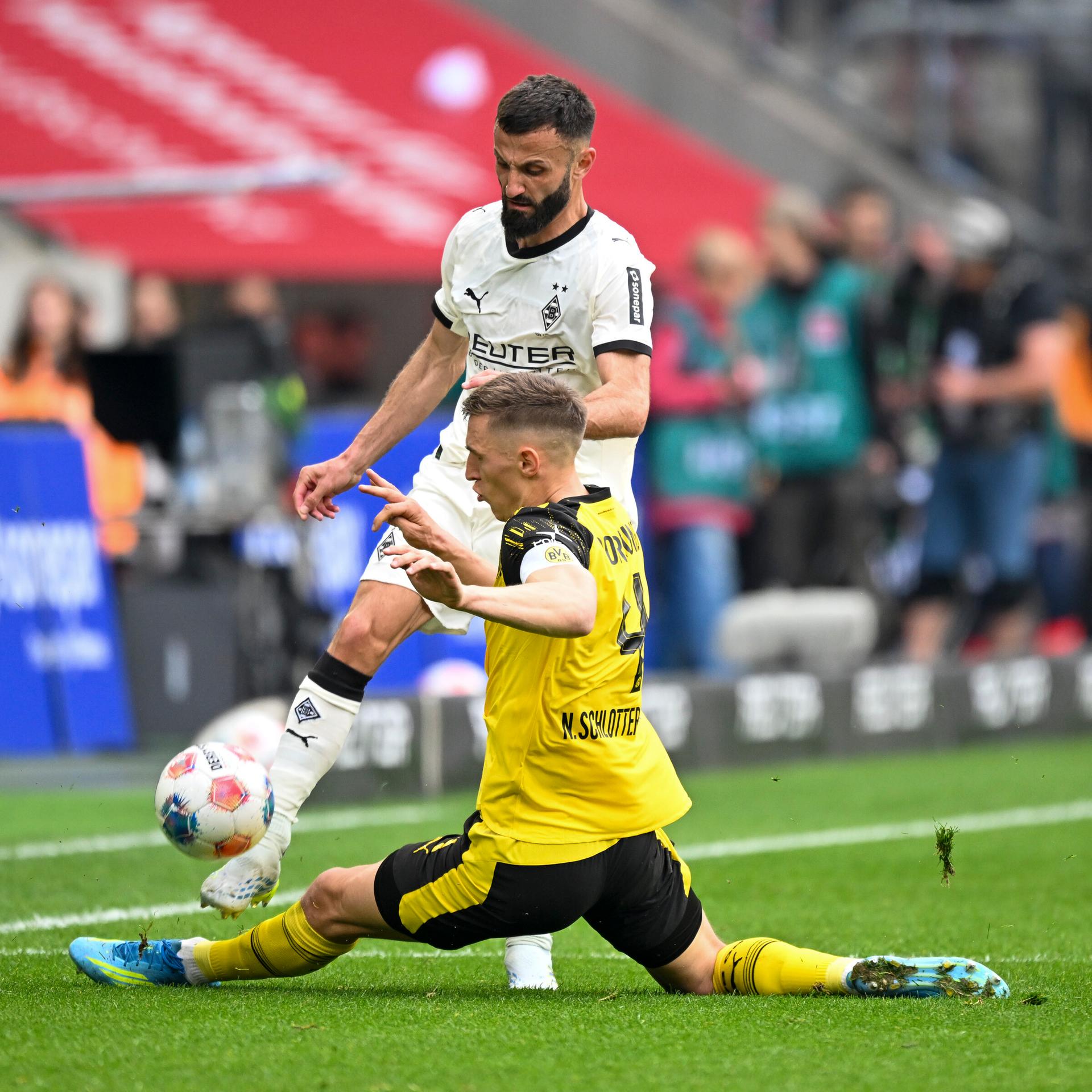 Der Fußballer Nico Schlotterbeck (Borussia Dortmund) grätscht vor dem Spieler Franck Honorat (Borussia Mönchengladbach) und versucht den Ball zu treffen.