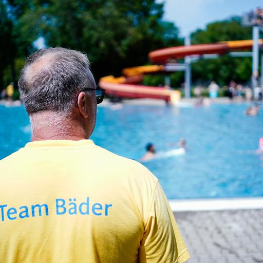 Ein Bademeister steht im Herzogenriedbad vor einem Schwimmbecken mit Wasserrutsche.