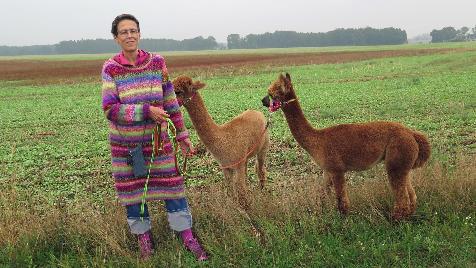 Schirin Schahbaz posiert mit zwei ihrer Alpakas auf einem Feld für ein Foto.