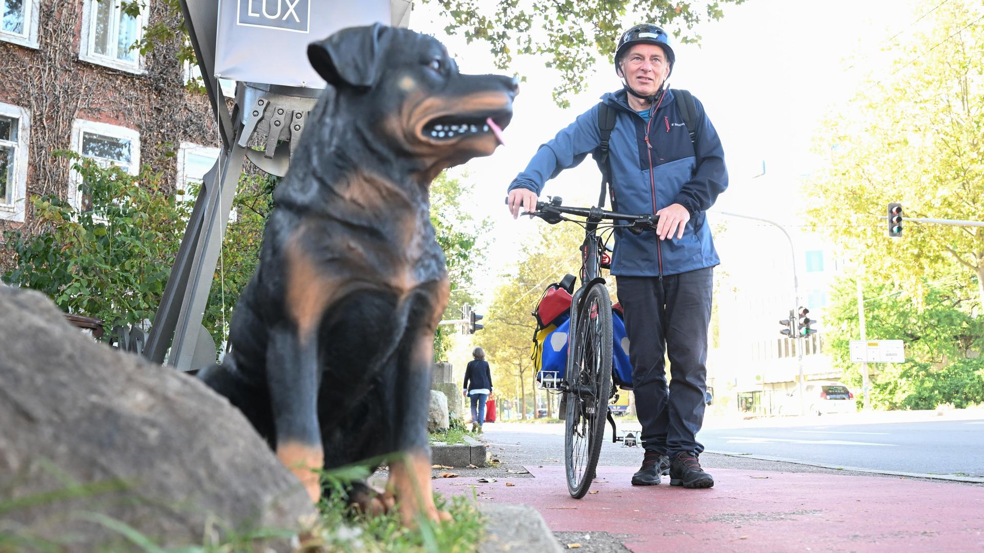 EIn Plastikhund, im Hintergrund ein Mann, der sein Rad auf dem Bürgersteig schiebt EIn Plastikhund, im Hintergrund ein Mann, der sein Rad auf dem Bürgersteig schiebt
