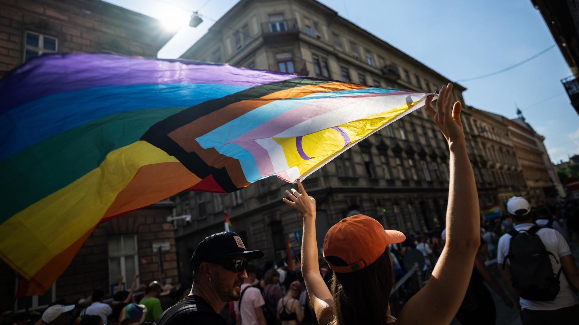 Eine Demonstrierende hält während einer Parade die Pride-Flagge in die Höhe.