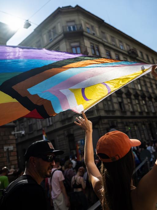 Eine Demonstrierende hält während einer Parade die Pride-Flagge in die Höhe.