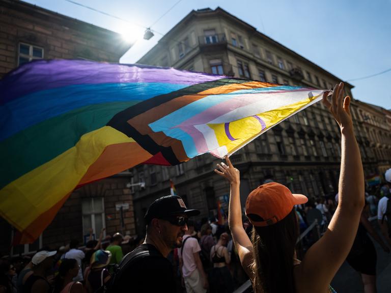 Eine Demonstrierende hält während einer Parade die Pride-Flagge in die Höhe.