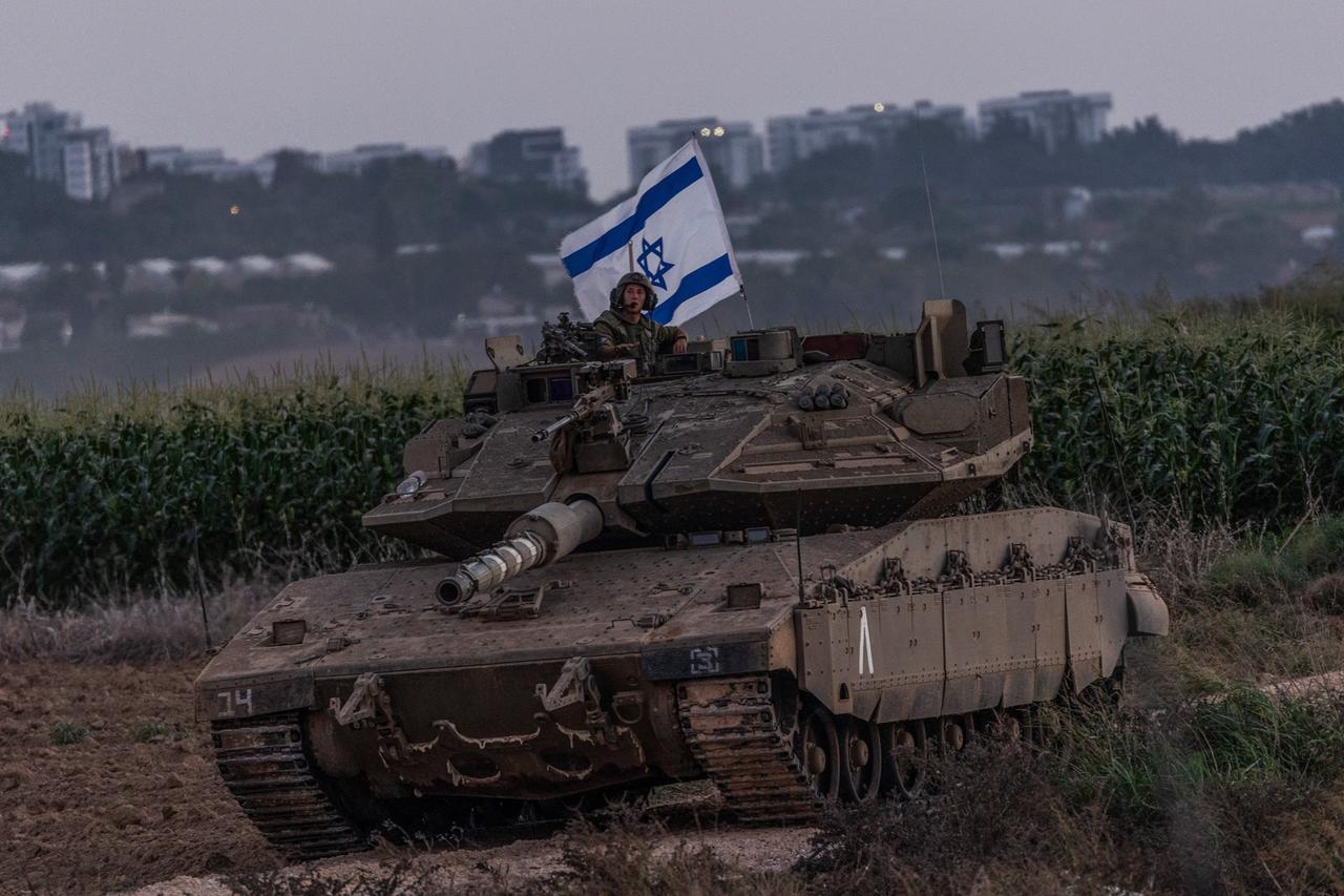 Ein Panzer, daraus schaut ein Soldat mit israelischer Flagge. Im Hintergrund ist besiedeltes Gebiet zu erkennen. 