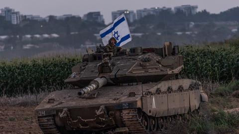 Ein Panzer, daraus schaut ein Soldat mit israelischer Flagge. Im Hintergrund ist besiedeltes Gebiet zu erkennen. 