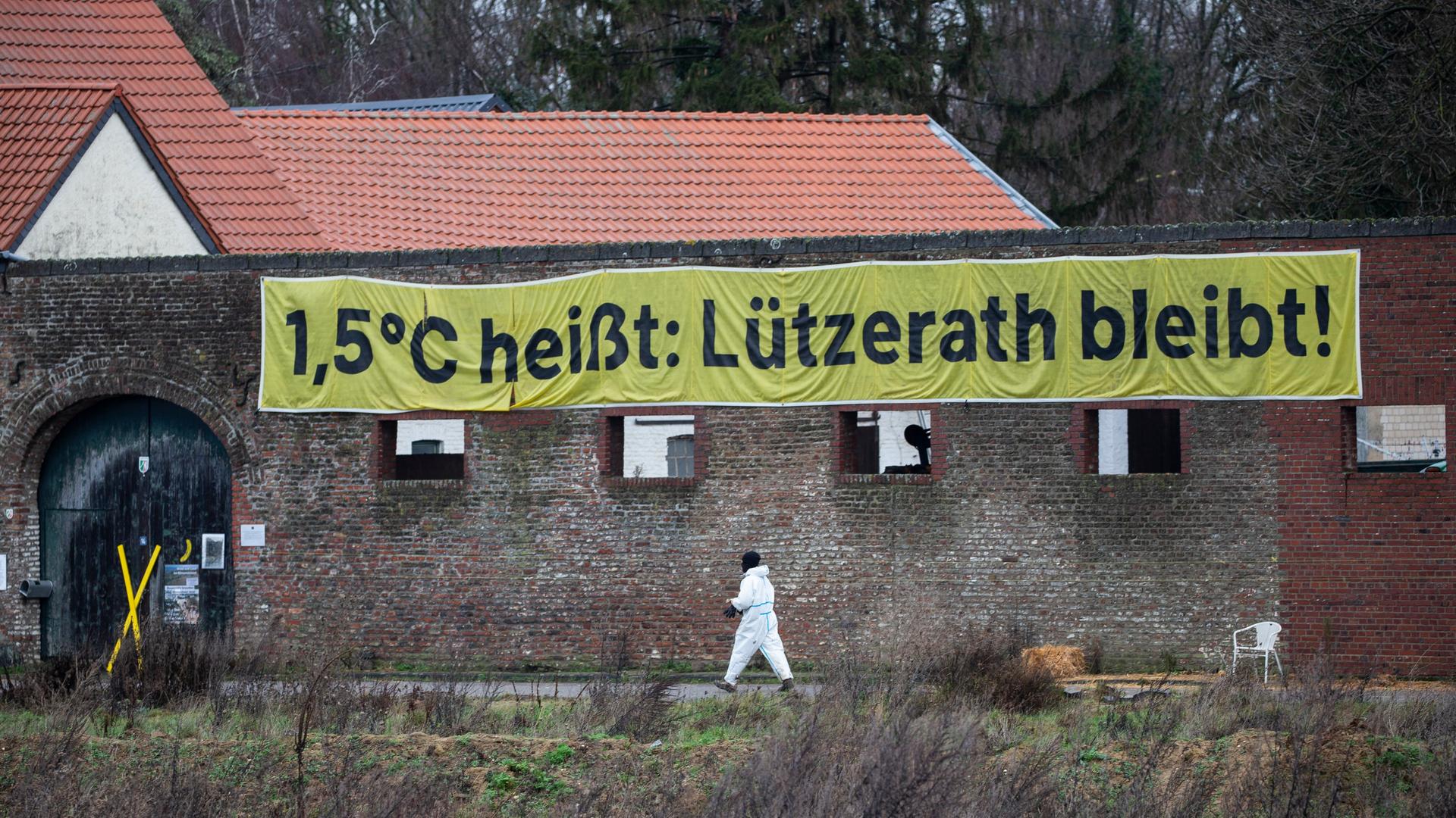Im Dorf Lützerath geht ein Aktivist vor einem ehemaligen Bauernhof vorbei. An dem Gebäude hängt ein Transparent mit der Aufschrift "1,5 C heißt: Lützerath bleibt!"