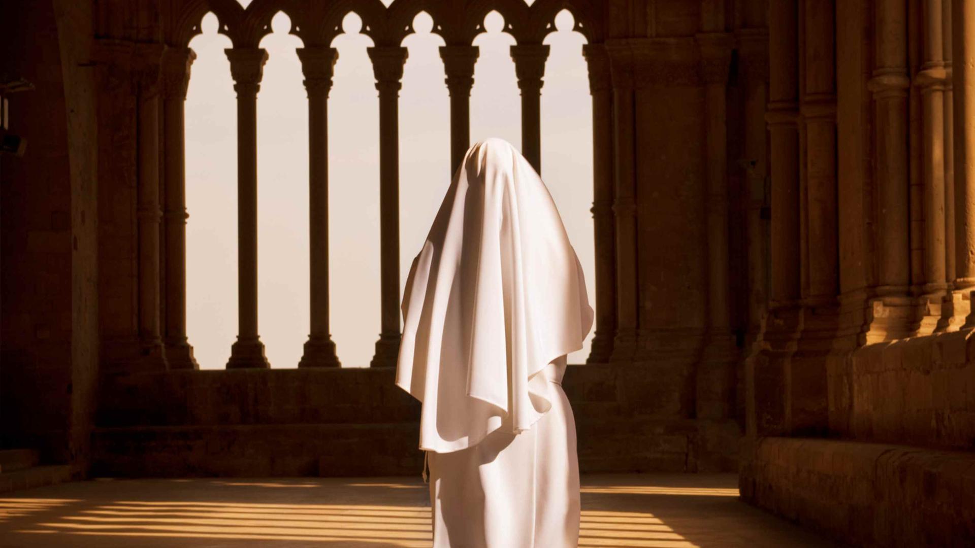Eine weiß gekleidete Nonne geht auf ein Kirchenfenster zu. Eine weiß gekleidete Nonne geht auf ein Kirchenfenster zu.