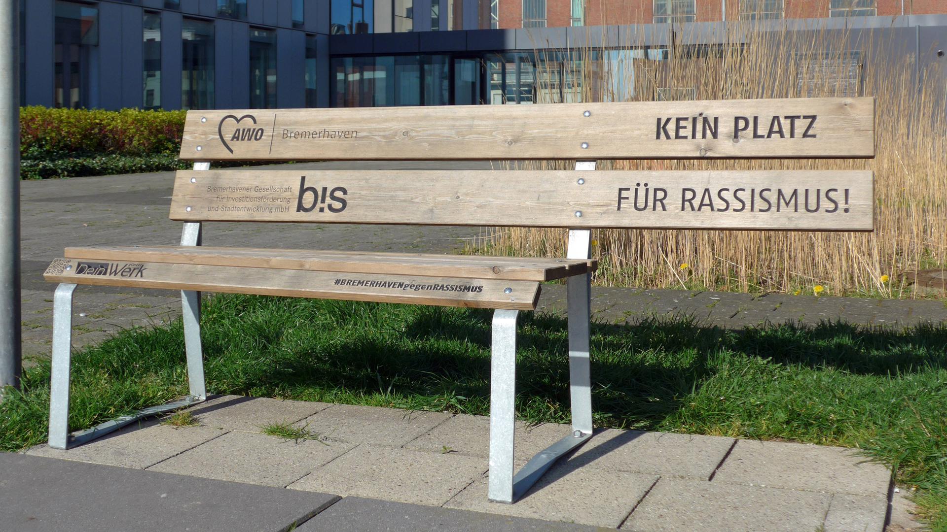 Die Rückenlehne einer Holzbank ragt über die Sitzfläche hinaus. Dort, wo niemand sitzen kann, steht auf der Lehne: "Kein Platz für Rassismus".