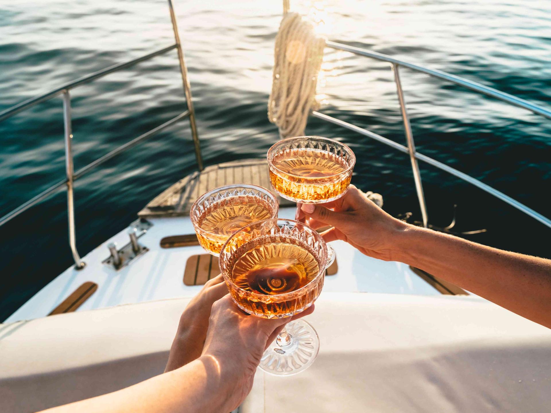 Auf dem Deck eines fahrenden Schiffes wird mit drei Champagnerschalen angestoßen.