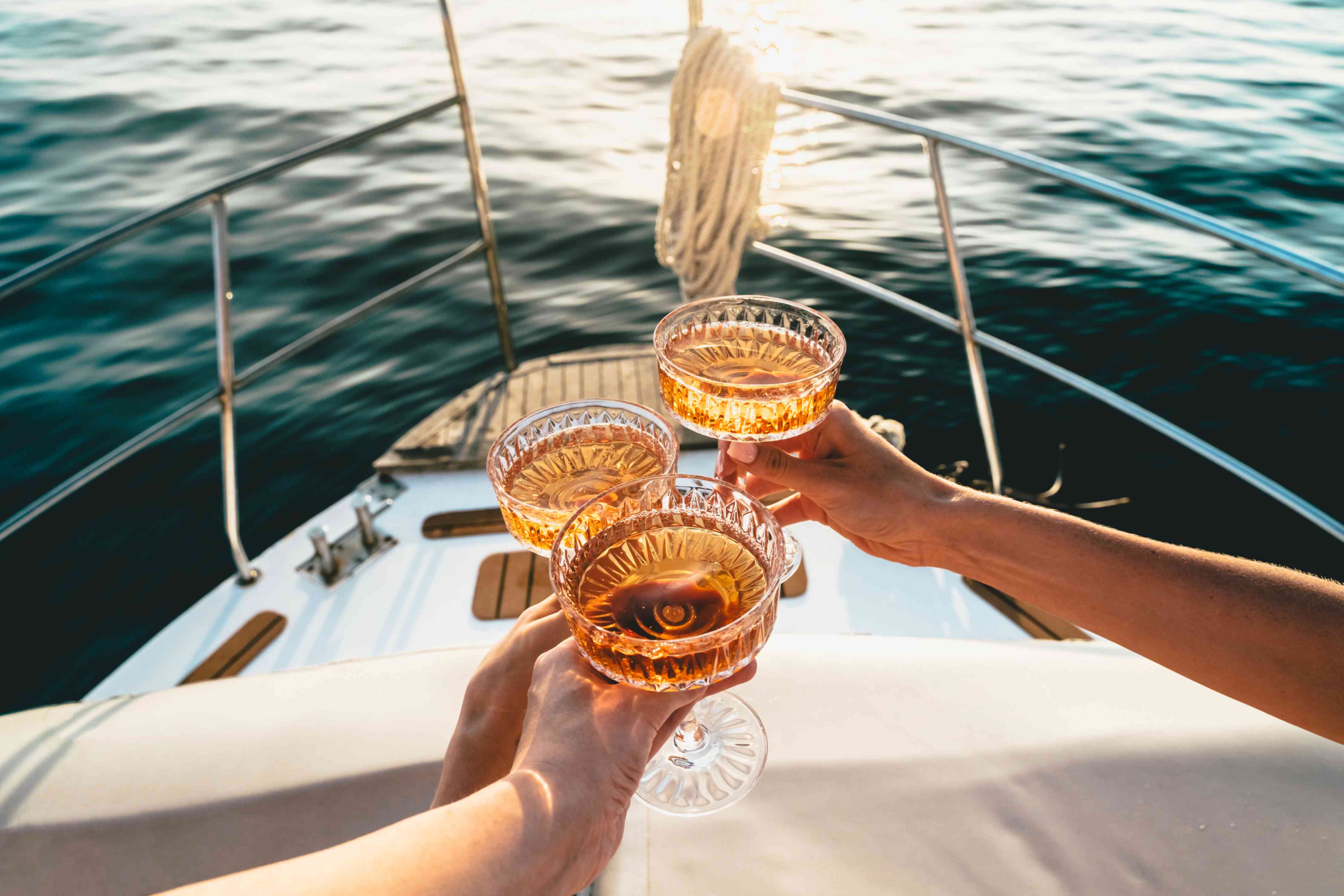 Auf dem Deck eines fahrenden Schiffes wird mit drei Champagnerschalen angestoßen.