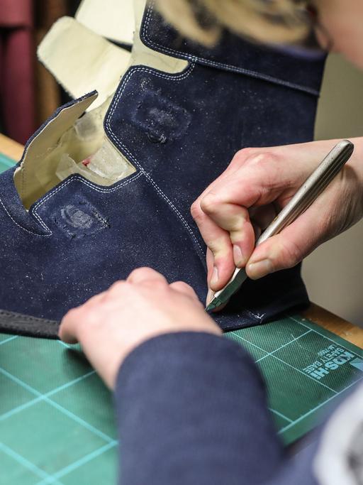 Eine Auszubildende zur Orthopädieschuhmacherin schneidet das Leder eines orthopädischen Schuhs zurecht.
