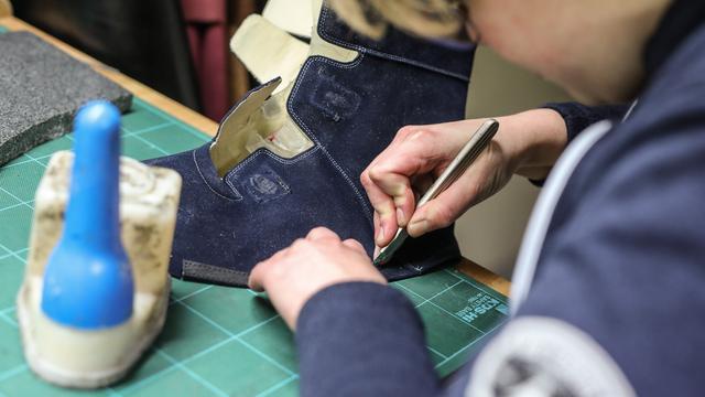 Eine Auszubildende zur Orthopädieschuhmacherin schneidet das Leder eines orthopädischen Schuhs zurecht.