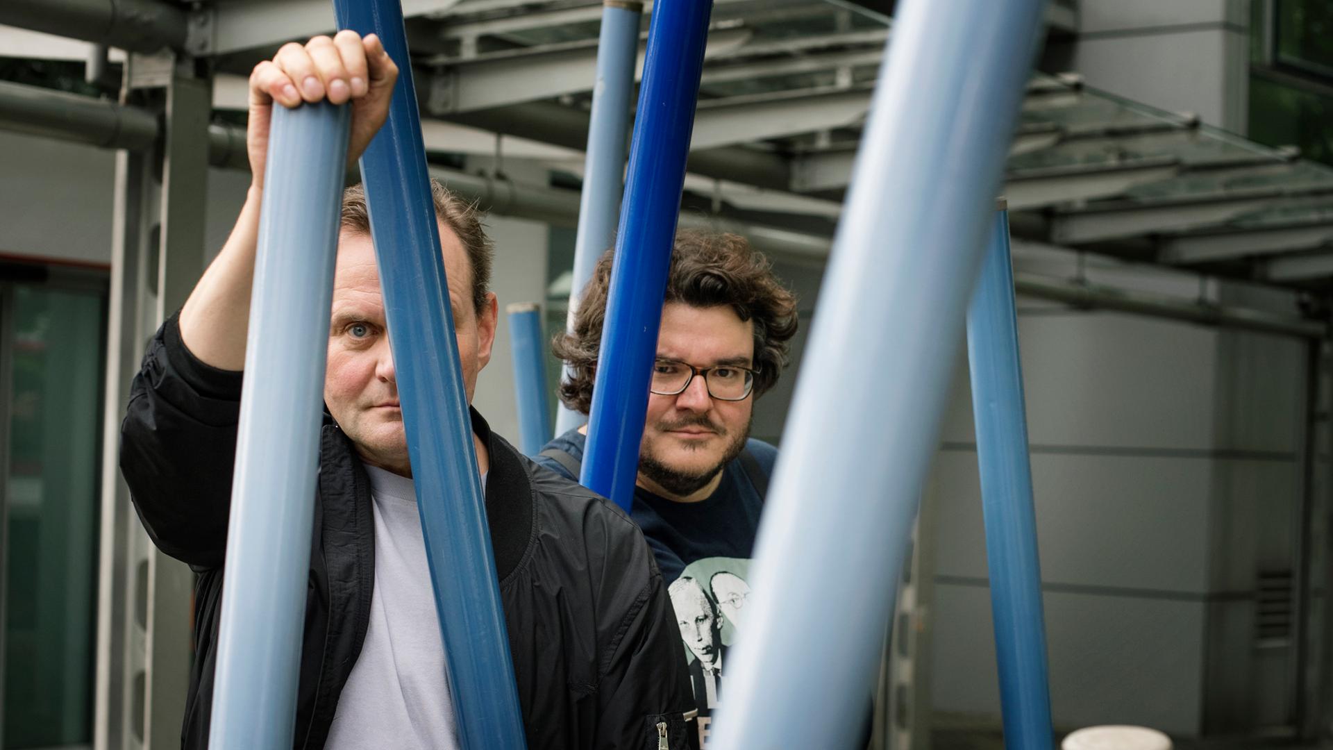 Devid Striesow und Axel Ranisch stehen unter einem Klettergerüst und schauen ernst in die Kamera Devid Striesow und Axel Ranisch stehen unter einem Klettergerüst und schauen ernst in die Kamera