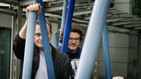 Devid Striesow und Axel Ranisch stehen unter einem Klettergerüst und schauen ernst in die Kamera