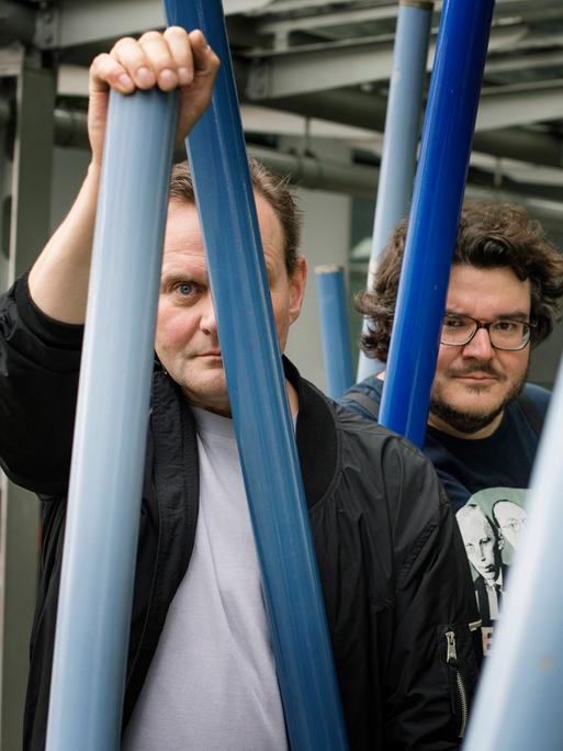 Devid Striesow und Axel Ranisch stehen unter einem Klettergerüst und schauen ernst in die Kamera